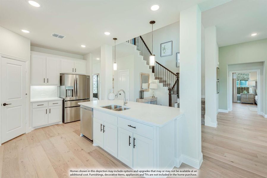Kitchen with white cabinets, island sink, stainless appliances, and light hardwood floors open to staircase