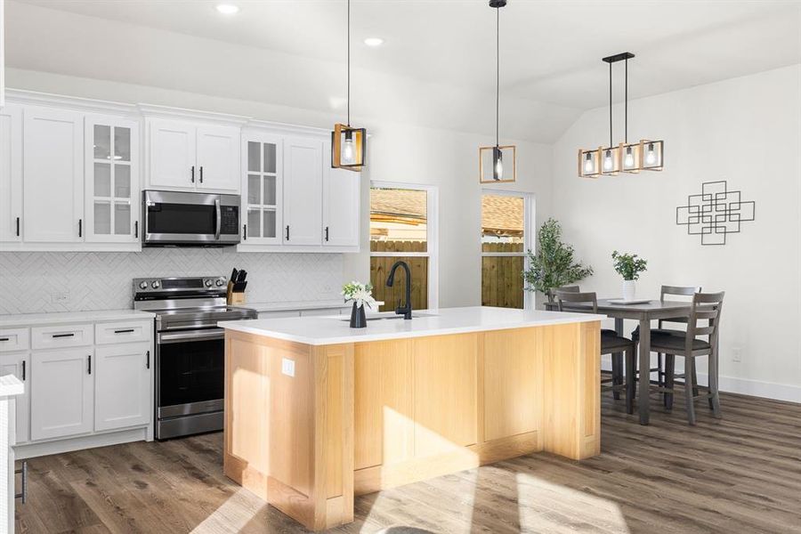 Kitchen featuring appliances with stainless steel finishes, a kitchen island with sink, white cabinets, dark hardwood / wood-style floors, and hanging light fixtures