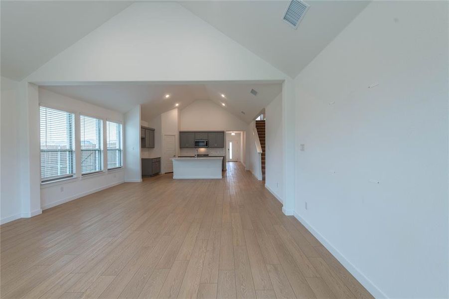 Unfurnished living room with stairway, light wood-style flooring, high vaulted ceiling, and baseboards
