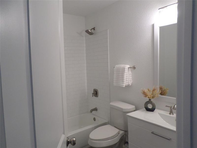 Bathroom featuring a white subway tile shower surround, brushed nickel shower fixtures, a white vanity with a single sink, and a framed mirror with overhead lighting