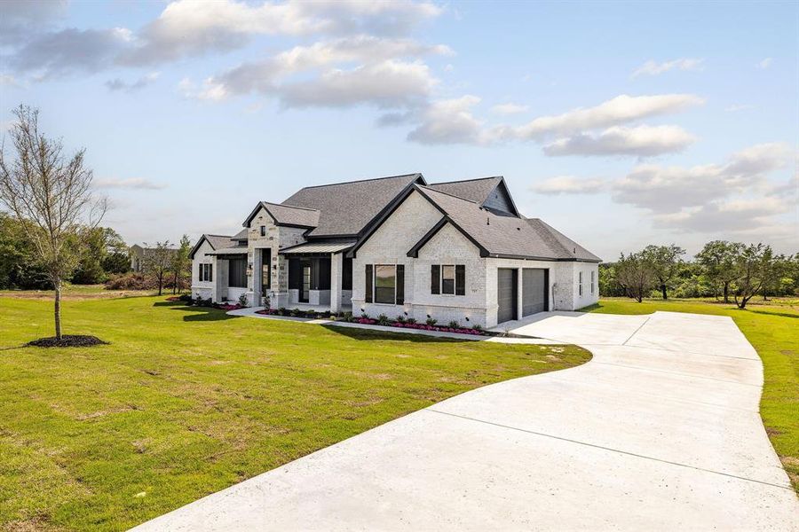 Modern farmhouse style home featuring an attached garage, driveway, stone siding, and a front yard