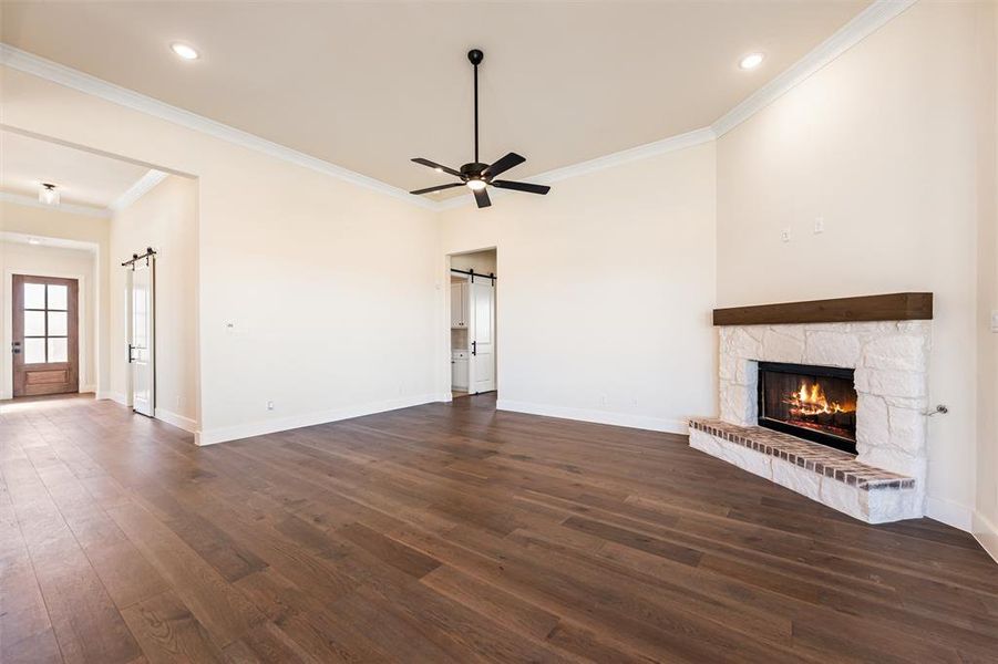Unfurnished living room featuring a barn door, dark wood finished floors, ceiling fan, a fireplace, and ornamental molding