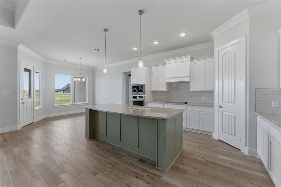 Expansive kitchen and dining area featuring a prominent island with pendant lighting, wood-finish flooring, white cabinetry, and recessed lighting