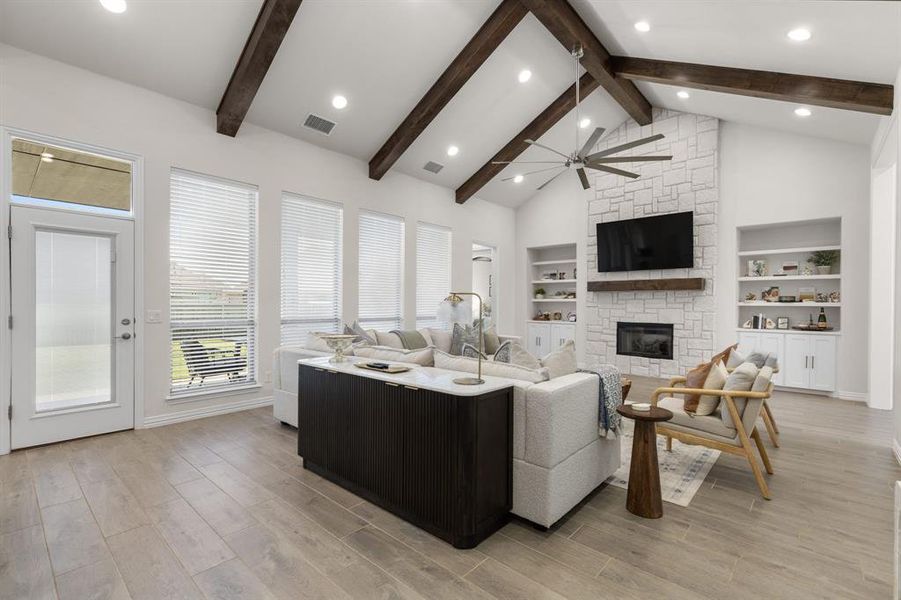 Living area with a fireplace, light wood-style flooring, high vaulted ceiling, ceiling fan, and built in features Living area with a fireplace, light wood-style flooring, high vaulted ceiling, ceiling fan, and built in features