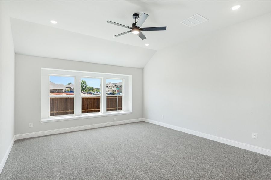 Empty bedroom with vaulted ceiling, ceiling fan, gray carpet, and triple window Empty bedroom with vaulted ceiling, ceiling fan, gray carpet, and triple window