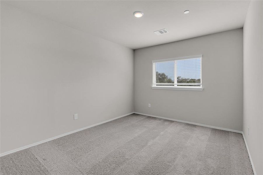 This is a bright 3rd bedroom featuring plush carpeting, a large window for natural light, and recessed lighting.