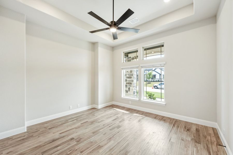 Empty room with hardwood floors, tray ceiling, ceiling fan, and large windows with natural light Empty room with hardwood floors, tray ceiling, ceiling fan, and large windows with natural light