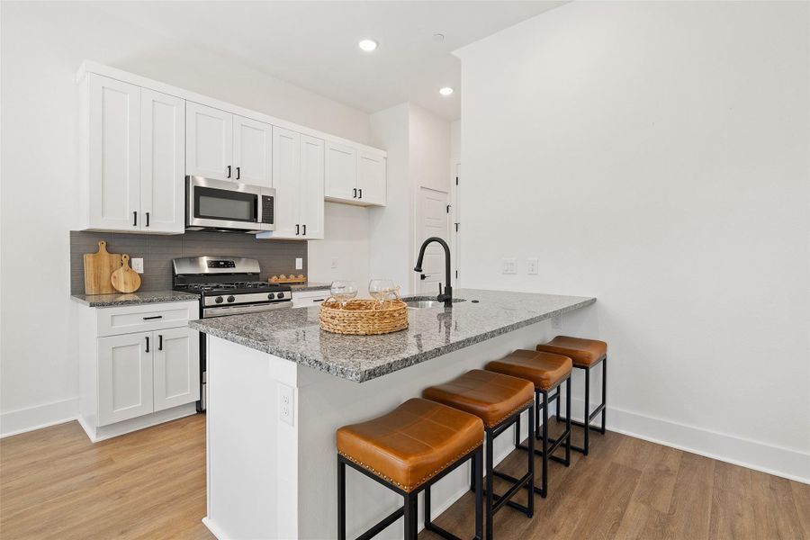Kitchen featuring a breakfast bar area, light stone countertops, white cabinetry, and recessed lighting Kitchen featuring a breakfast bar area, light stone countertops, white cabinetry, and recessed lighting
