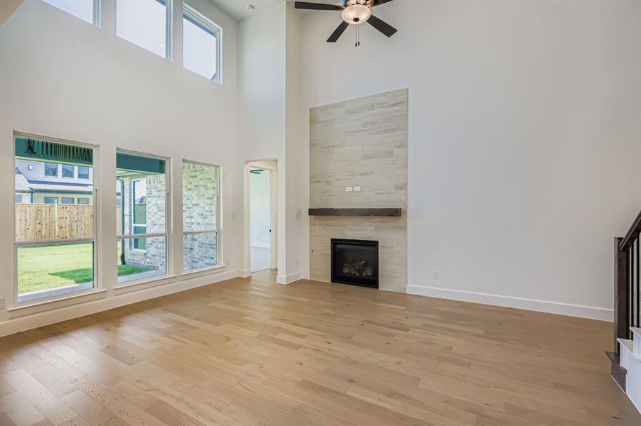 Unfurnished living room featuring light wood-style flooring, a tiled fireplace, ceiling fan, and a towering ceiling