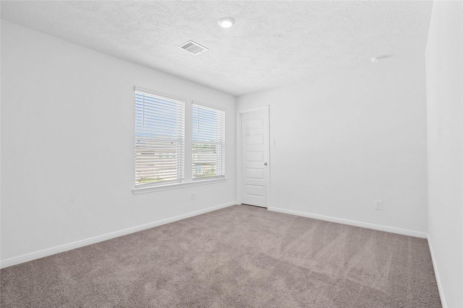 This secondary bedroom offers comfort and style with plush carpeting, neutral paint tones, recessed lighting, large windows with blinds, and a walk-in closet.
