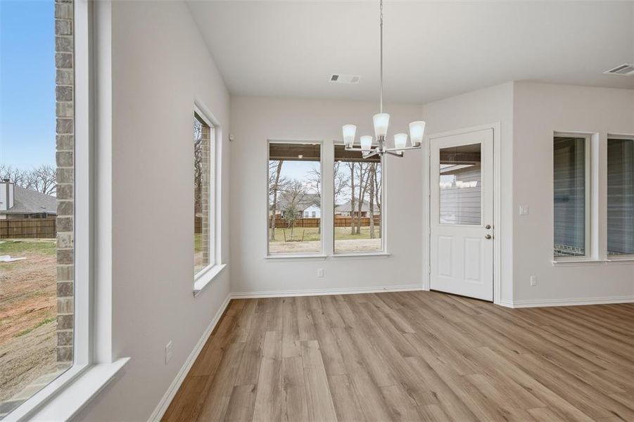 Unfurnished dining area featuring a chandelier, light wood finished floors, and healthy amount of natural light Unfurnished dining area featuring a chandelier, light wood finished floors, and healthy amount of natural light