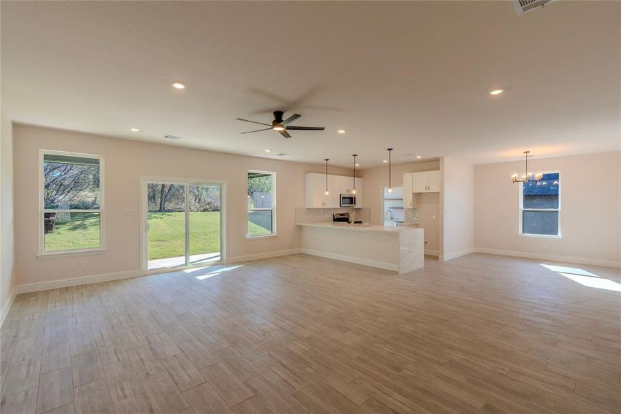 Unfurnished living room featuring ceiling fan with notable chandelier and light hardwood / wood-style flooring