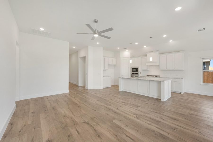Open-concept living area and kitchen with white cabinets, center island, and light wood floors with ceiling fan Open-concept living area and kitchen with white cabinets, center island, and light wood floors with ceiling fan