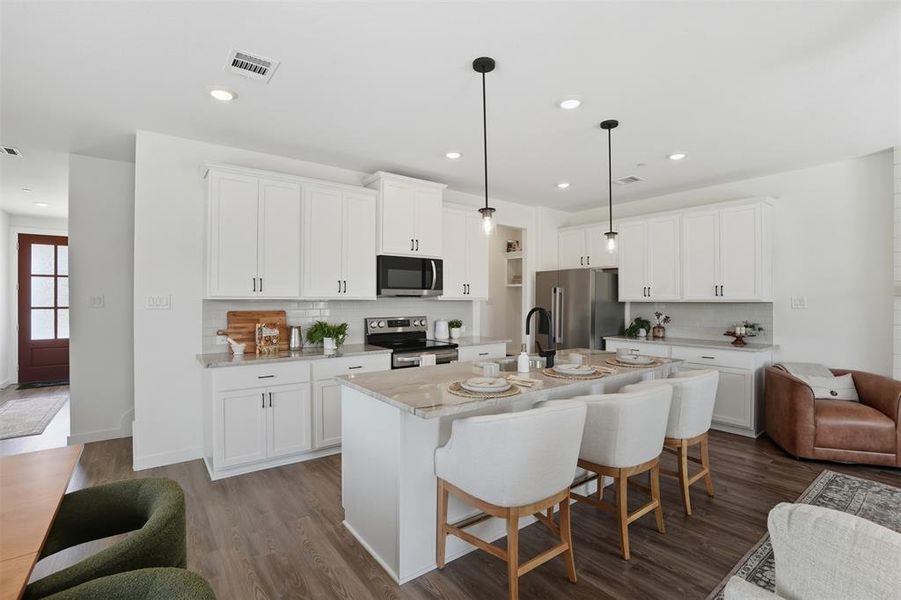 Kitchen featuring decorative backsplash, dark wood finished floors, a breakfast bar area, stainless steel appliances, and light stone counters Kitchen featuring decorative backsplash, dark wood finished floors, a breakfast bar area, stainless steel appliances, and light stone counters