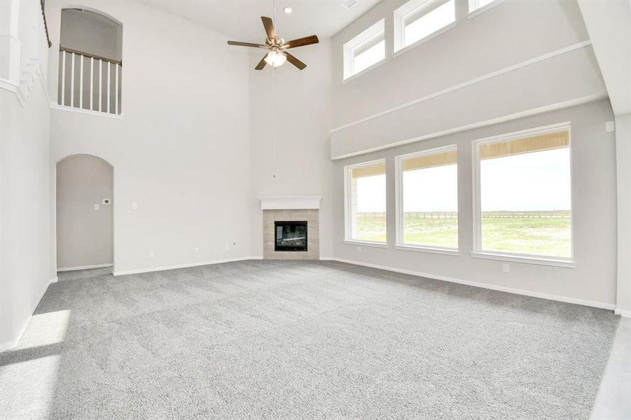 The living room features plush carpet, fireplace, high ceilings, large windows, and a ceiling fan.