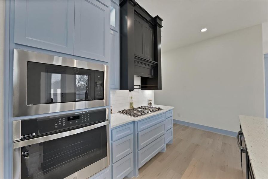 Kitchen with stainless steel appliances, light stone counters, light wood-type flooring, backsplash, and recessed lighting