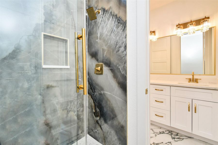 Luxury redefined in the primary bath, showcasing a walk-in shower with floor-to-ceiling stone slabs that mimic natural agate. Brushed gold shower hardware, a built-in niche, and high-contrast marble flooring elevate the space to a true home spa.