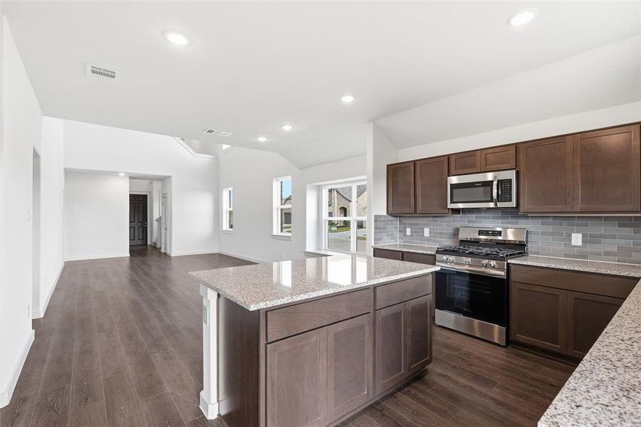 Kitchen with appliances with stainless steel finishes, dark brown cabinets, light stone countertops, dark wood-style flooring, and decorative backsplash Kitchen with appliances with stainless steel finishes, dark brown cabinets, light stone countertops, dark wood-style flooring, and decorative backsplash