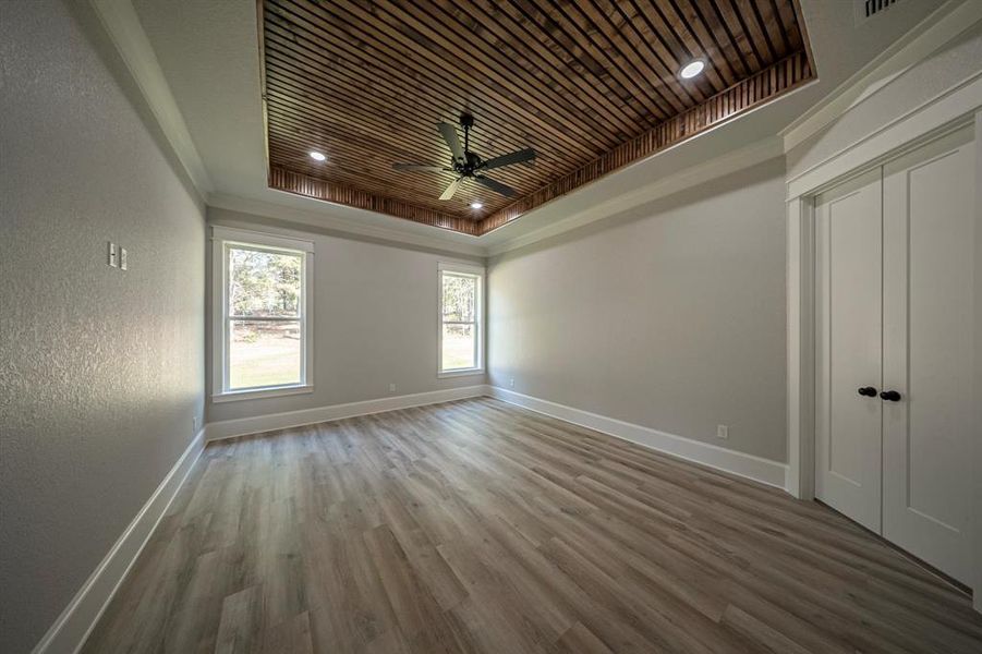Empty room featuring a raised ceiling, wood finished floors, ceiling fan, wooden ceiling, and crown molding Empty room featuring a raised ceiling, wood finished floors, ceiling fan, wooden ceiling, and crown molding