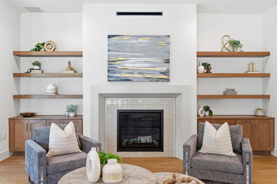 Living room with light wood finished floors, a tiled fireplace, and built in shelves