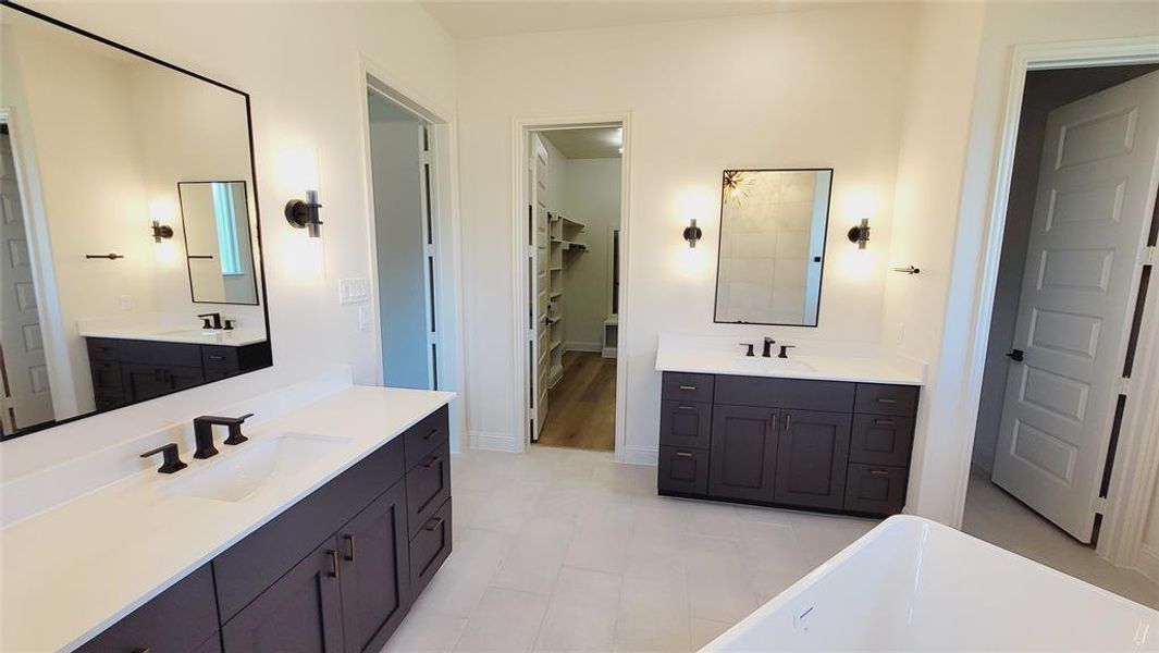 Spacious bathroom featuring dual dark wood vanities with white countertops, matte black plumbing fixtures, and wall-mounted mirrors with integrated sconce lighting