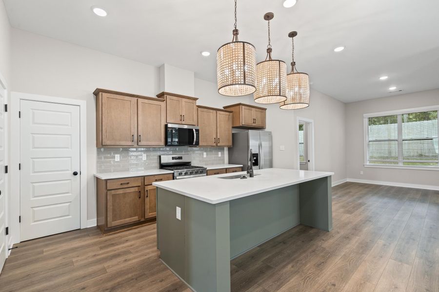 Kitchen featuring tasteful backsplash, an island with sink, appliances with stainless steel finishes, hanging light fixtures, and brown cabinets