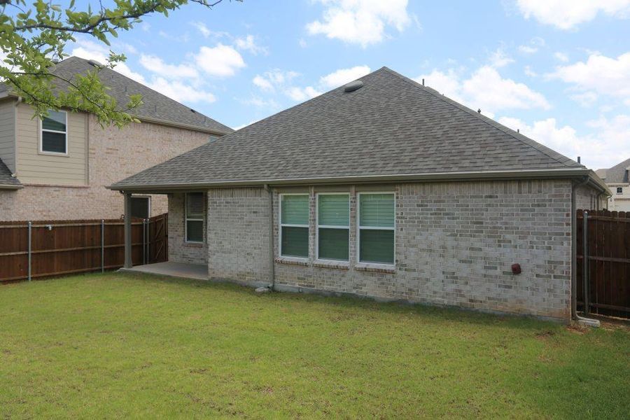 Expansive green lawn with a covered patio, brick exterior, and a privacy fence