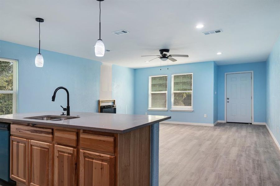 Kitchen featuring light wood-style floors, decorative light fixtures, open floor plan, a ceiling fan, and brown cabinets Kitchen featuring light wood-style floors, decorative light fixtures, open floor plan, a ceiling fan, and brown cabinets