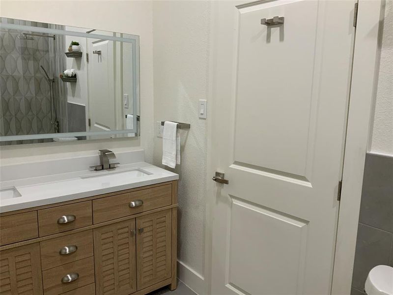 Full bathroom with a textured wall, double vanity, and a shower Full bathroom with a textured wall, double vanity, and a shower