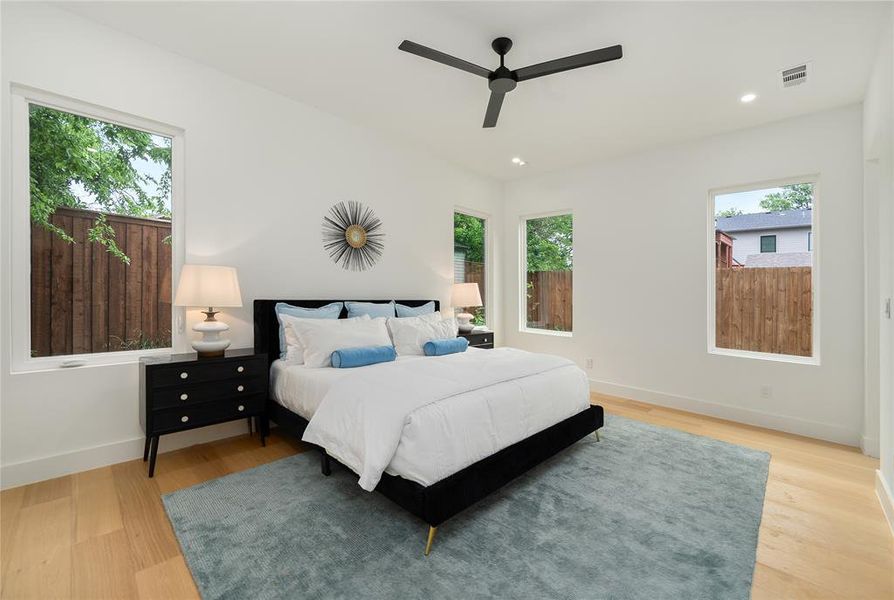 This bedroom features light wood flooring, several windows providing natural light, and recessed lighting