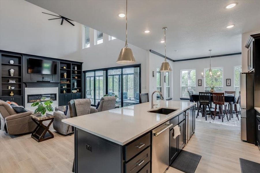 Kitchen featuring open floor plan, a glass covered fireplace, decorative light fixtures, light tile flooring, and a high ceiling