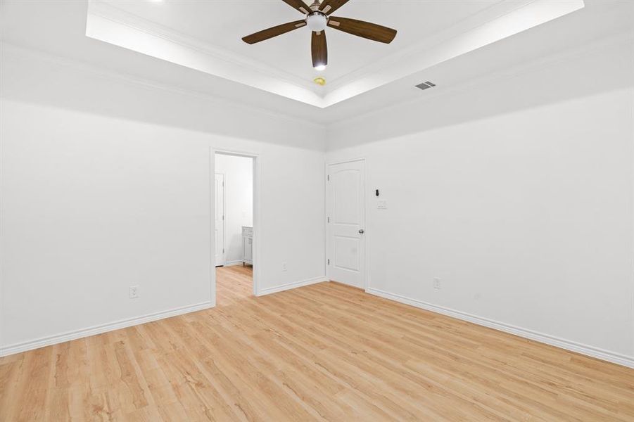Empty room with ceiling fan, a raised ceiling, crown molding, and light wood-style floors Empty room with ceiling fan, a raised ceiling, crown molding, and light wood-style floors