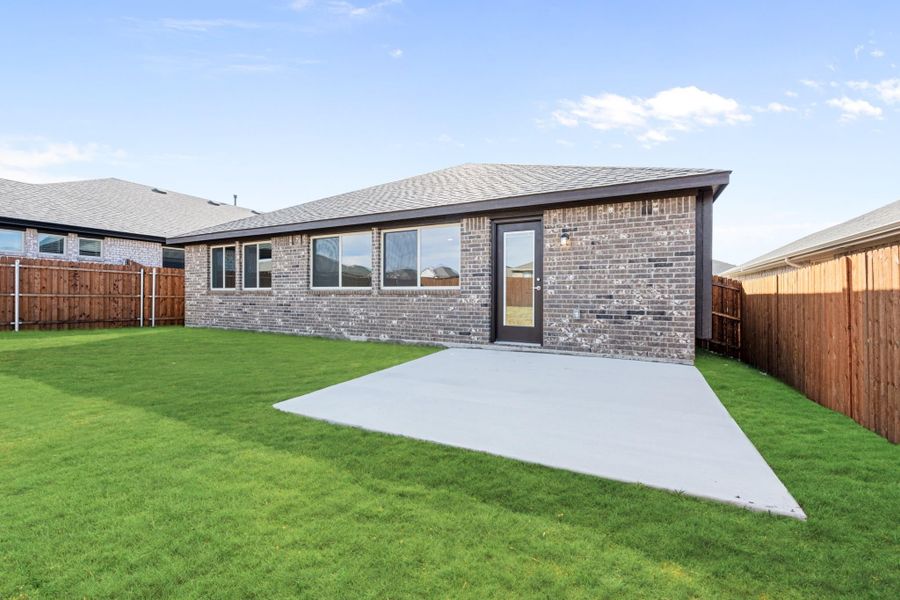 Backyard of brick home with concrete patio, green lawn, and wood privacy fence Backyard of brick home with concrete patio, green lawn, and wood privacy fence