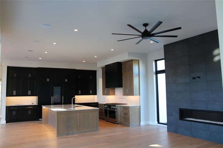 Kitchen with light hardwood / wood-style flooring, an island with sink, double oven range, extractor fan, and a fireplace