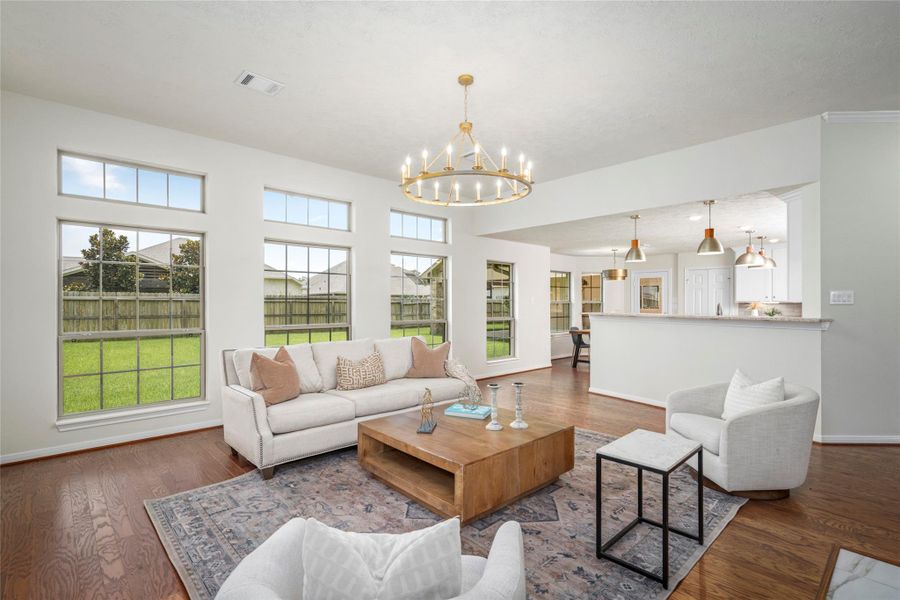 Spacious open-concept living area with soaring ceilings and an elegant gold wagon-wheel chandelier, flowing seamlessly into the kitchen with an abundance of natural light from oversized windows. Spacious open-concept living area with soaring ceilings and an elegant gold wagon-wheel chandelier, flowing seamlessly into the kitchen with an abundance of natural light from oversized windows.