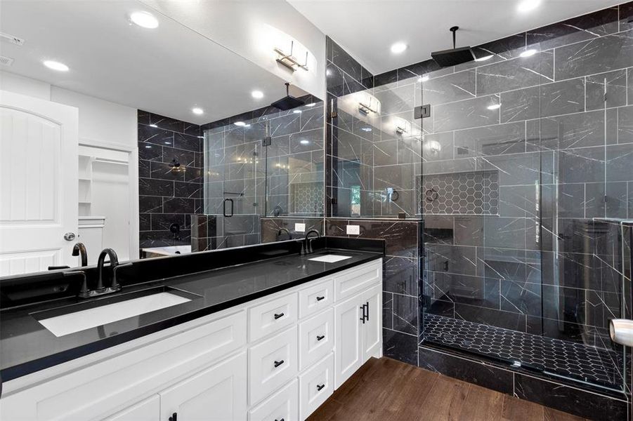 Bathroom with a marble finish shower, double vanity, dark wood-style flooring, tile walls, and recessed lighting