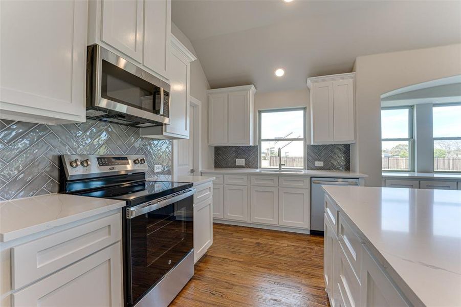 Kitchen featuring decorative backsplash, appliances with stainless steel finishes, vaulted ceiling, light hardwood / wood-style flooring, and white cabinets