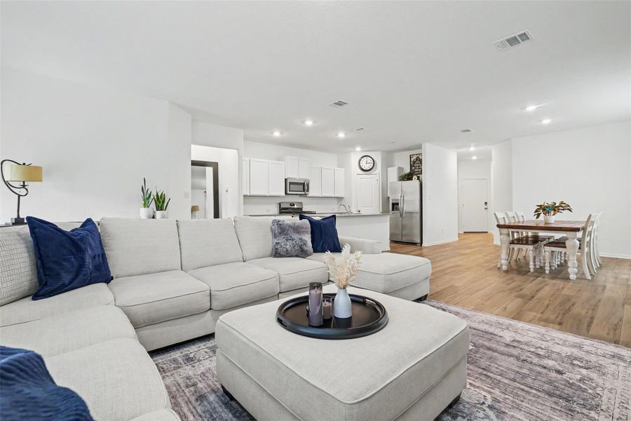 Open-concept living space featuring wood-finish flooring, recessed lighting, white walls, and a kitchen with white cabinetry and stainless steel appliances