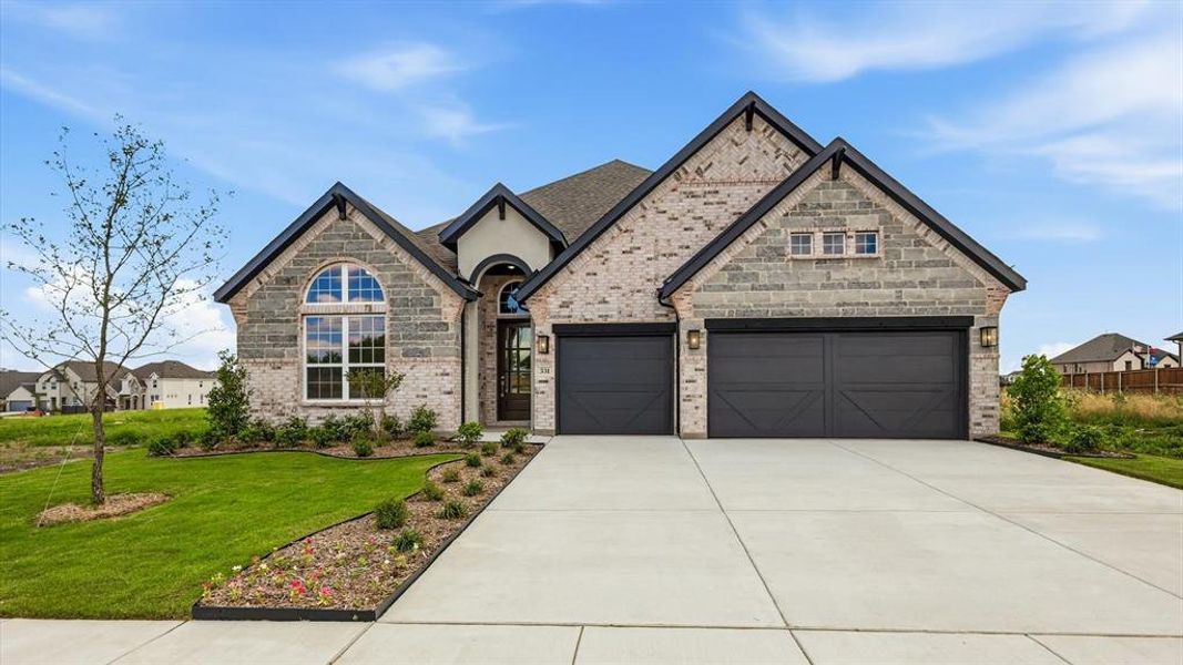 Contemporary architectural style featuring a multi-toned brick and stone facade, arched entry, two-car garage with carriage-style doors, a concrete driveway, and landscaped front yard with a young tree