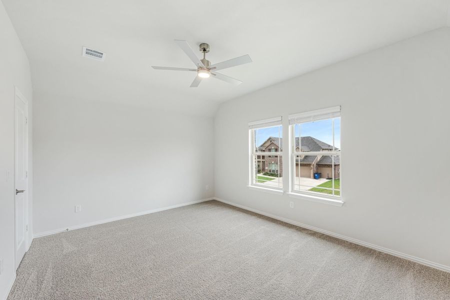 Empty bedroom with vaulted ceiling, ceiling fan, carpet flooring, and double windows overlooking neighborhood homes. Empty bedroom with vaulted ceiling, ceiling fan, carpet flooring, and double windows overlooking neighborhood homes.