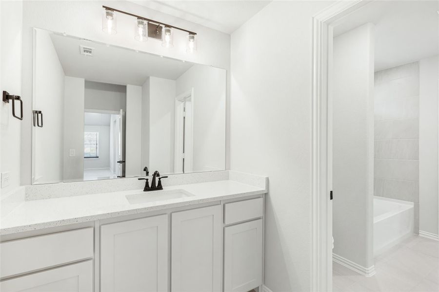 Bathroom with white vanity, quartz countertop, large mirror, and tiled soaking tub in adjacent alcove
