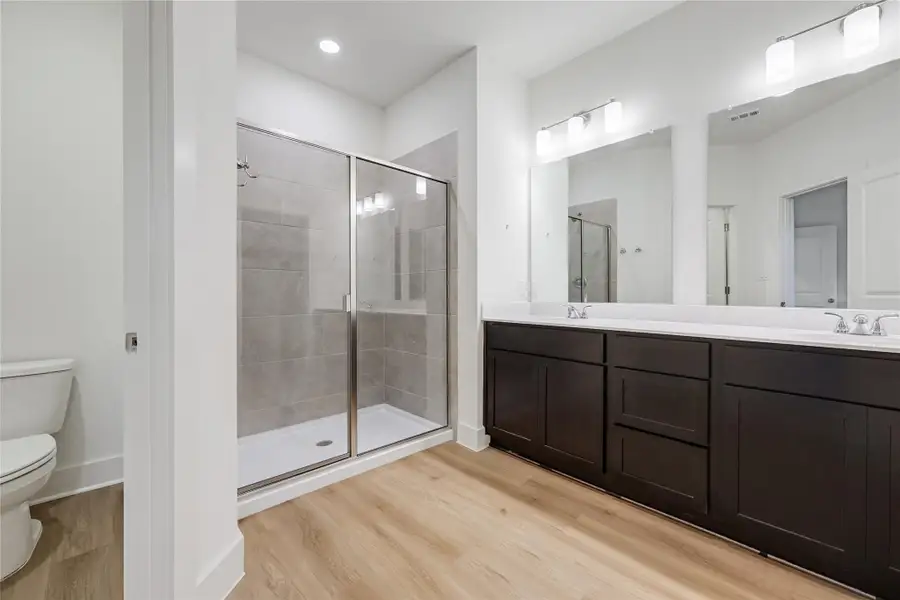 Full bathroom featuring a stall shower, double vanity, light wood-style flooring, and recessed lighting Full bathroom featuring a stall shower, double vanity, light wood-style flooring, and recessed lighting