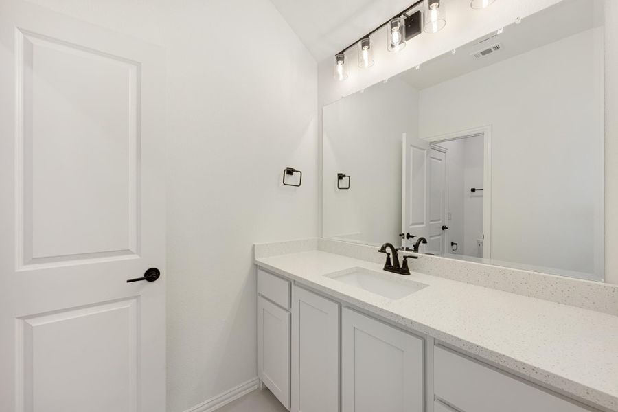 Bathroom vanity with white cabinets, quartz countertop, single sink, and large mirror with industrial-style light fixtures above Bathroom vanity with white cabinets, quartz countertop, single sink, and large mirror with industrial-style light fixtures above