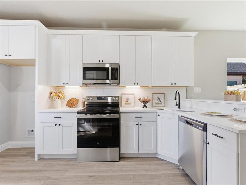 Kitchen featuring appliances with stainless steel finishes, decorative backsplash, white cabinets, and light wood-style flooring Kitchen featuring appliances with stainless steel finishes, decorative backsplash, white cabinets, and light wood-style flooring