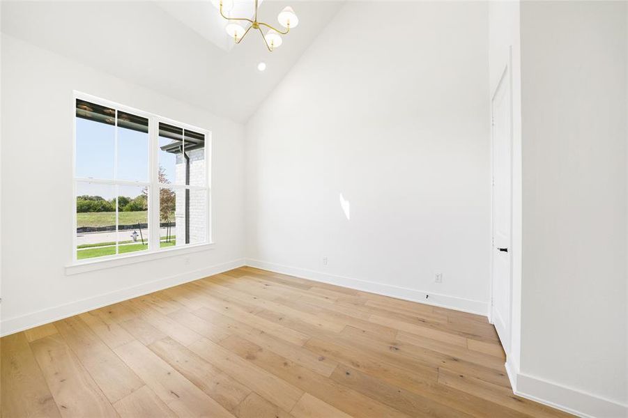 Empty room with high vaulted ceiling, a chandelier, light wood-style flooring, and recessed lighting