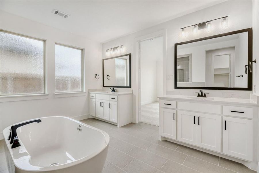 Bathroom featuring a freestanding bath, two vanities, and light tile patterned floors
