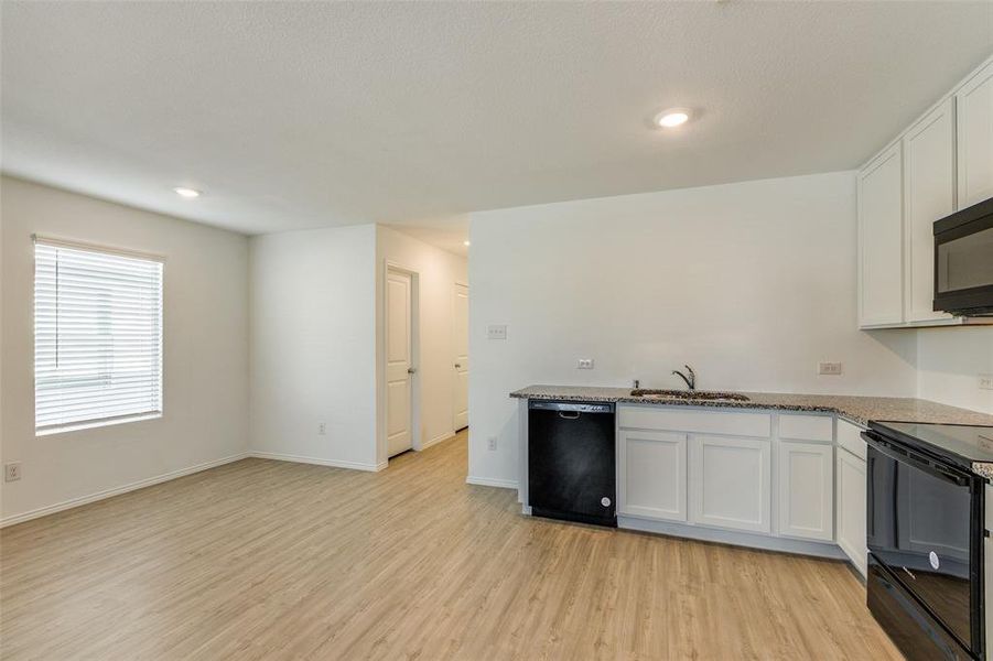 Kitchen with black appliances, light hardwood / wood-style floors, white cabinets, and light stone counters