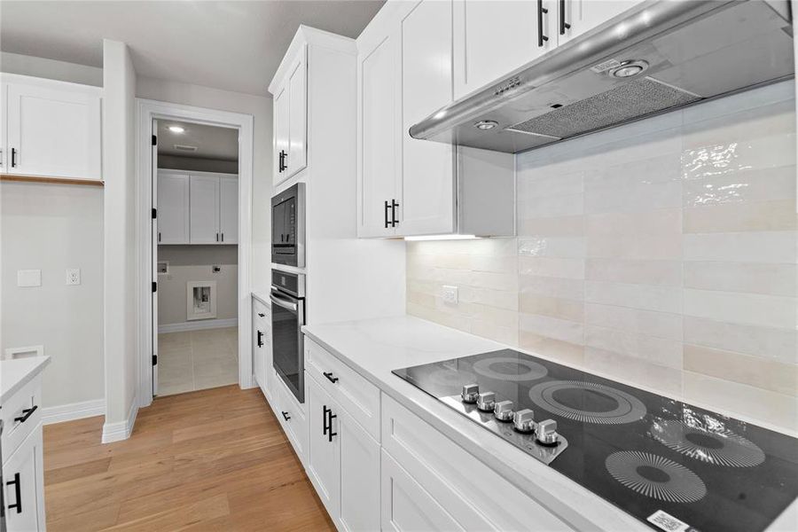 Kitchen featuring white cabinetry, SS appliances, light counters, decorative backsplash, and light hardwood floors