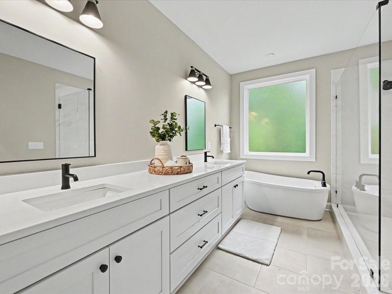 Luxurious primary bath offers a dual-sink vanity, oversized walk-in tile shower, and relaxing freestanding soaking tub.