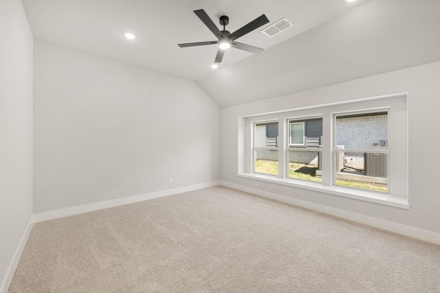 Empty bedroom with vaulted ceiling, ceiling fan, carpet flooring, and large triple-pane window Empty bedroom with vaulted ceiling, ceiling fan, carpet flooring, and large triple-pane window